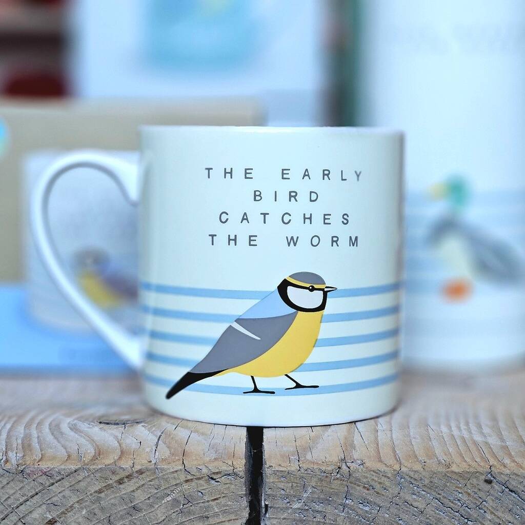 Mug with a bird illustration and text 'The early bird catches the worm' on a wooden surface.